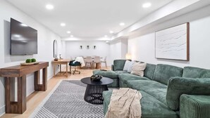 En moderne stue med en grøn sofa, et sofabord og et fjernsyn ophængt på væggen.