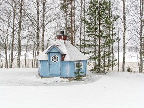 Pieni, yhden kerroksen korkuinen puinen rakennus, jonka katto on lumen peitossa, ja jonka ympärillä on metsä.
