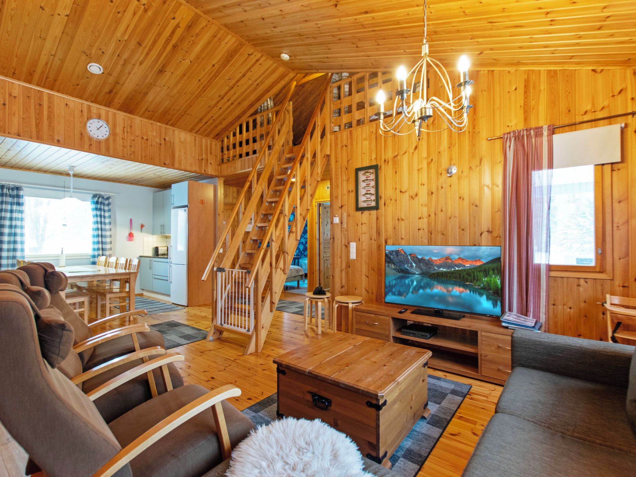 A wooden interior with a staircase, a dining area, a living room with a TV, and a cozy fireplace.