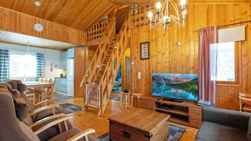 A wooden interior with a staircase, a dining area, a living room with a TV, and a cozy fireplace.