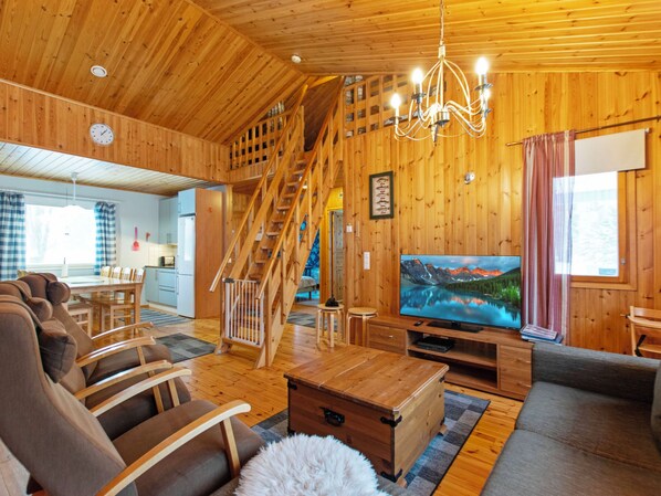 A wooden interior with a staircase, a dining area, a living room with a TV, and a cozy fireplace.