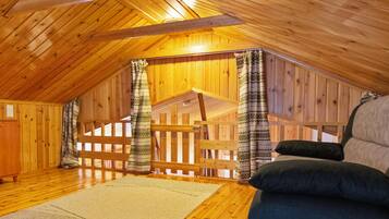 Ein Holzinnenraum mit schrägem Dach, einer Holztreppe und einem Sofa.