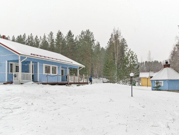 A snow-covered landscape with a blue building featuring a porch and a person walking in the distance.