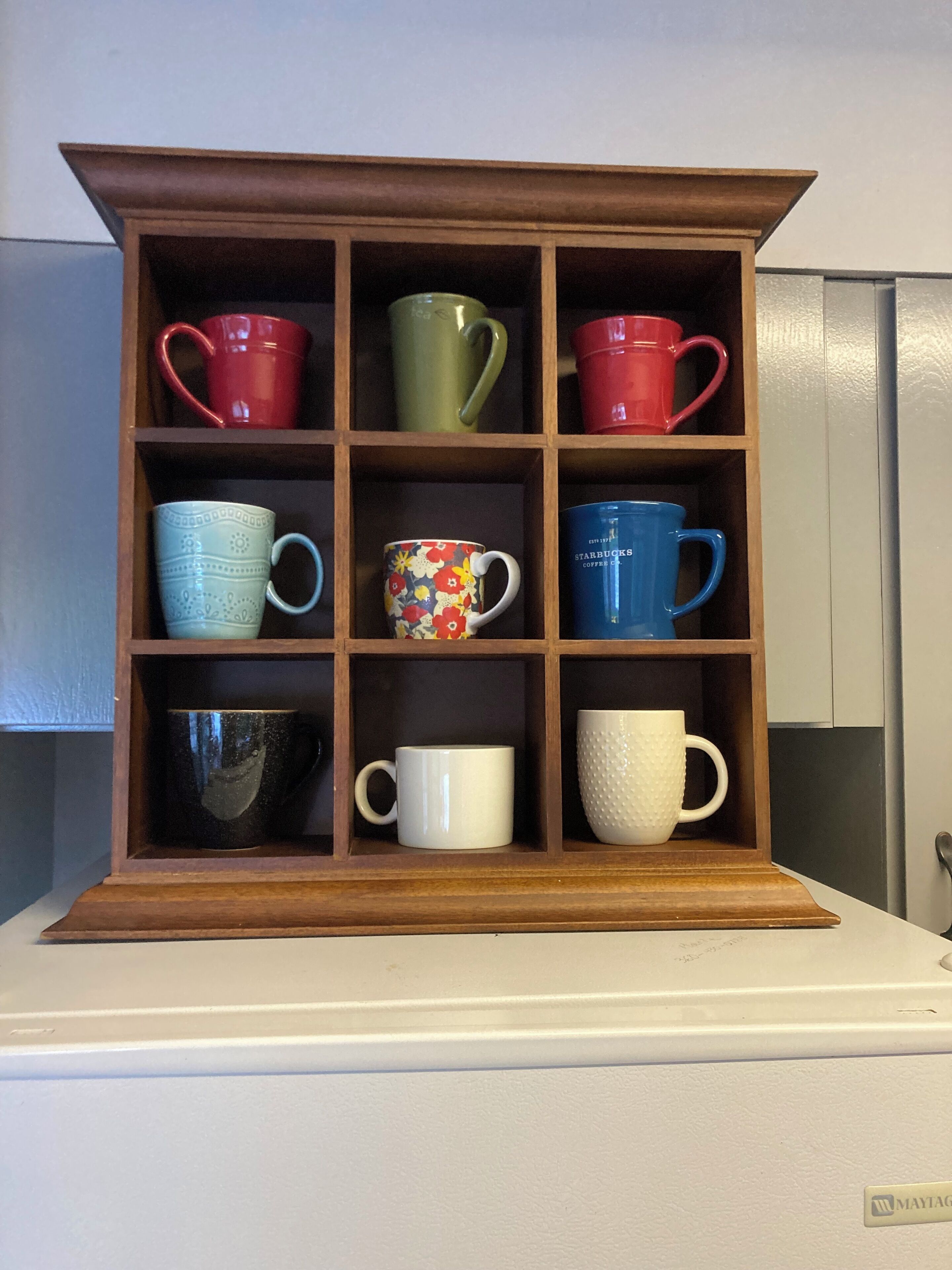 Un mueble de madera con varios compartimentos, cada uno con una taza de diferente color.
