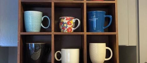 Un mueble de madera con varios compartimentos, cada uno con una taza de diferente color.