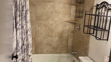 A bathroom with a bathtub, toilet, and sink. There is a shower curtain, a towel rack, and a shelf with toiletries.