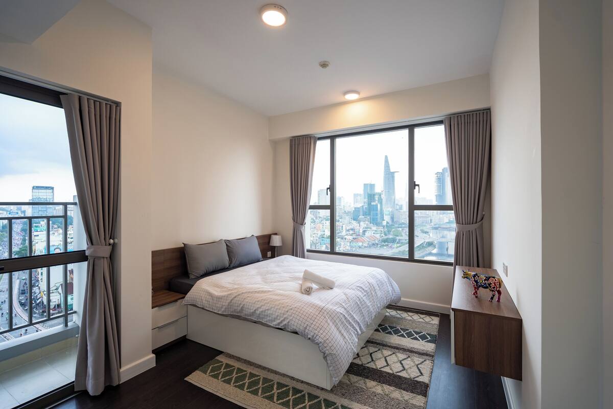 Een moderne hotelkamer met een groot bed, uitzicht op de stad en een klein bureau met een decoratief object.