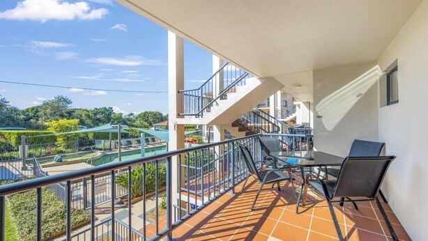 Uma varanda com vista para uma piscina, mobiliário de exterior e uma escadaria que leva a um andar superior.