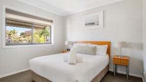 Quarto bem arrumado com uma cama grande, duas mesas de cabeceira, uma janela com vista e um quadro na parede.