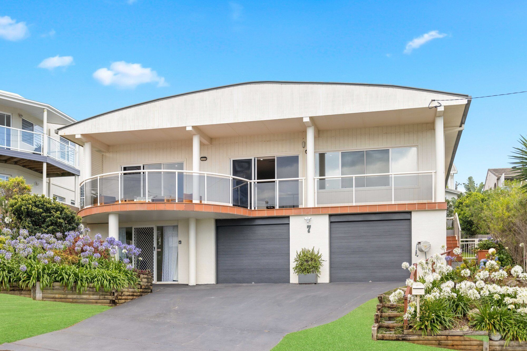 A modern two-story house with a curved roof, a balcony on the upper floor, and a garage.
