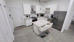 Una cocina moderna con armarios blancos, una isla central con taburetes, electrodomésticos de acero inoxidable y una lámpara original en forma de espiral.