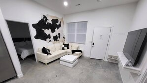 Una sala de estar moderna con un sofá seccional, una mesa de centro, un cuadro abstracto grande, un televisor y una puerta.