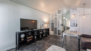 A modern living room with a flat-screen TV, a black entertainment unit, a glass coffee table, and a grey carpet.