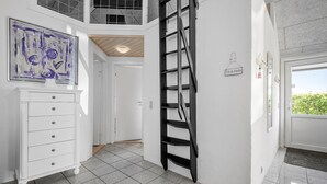 A hallway with a white dresser, a black metal ladder, and a door with a sign reading "Vi er pa stranden" (We are on the beach).