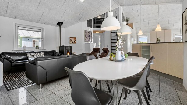 A modern living room with a black leather sofa, a white dining table with chairs, and a kitchen area in the background.