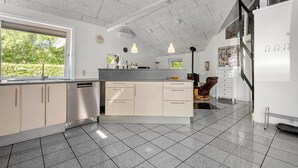 A modern kitchen with a large island, stainless steel appliances, and a view of greenery outside.