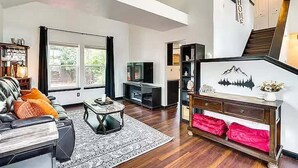 A modern living room with a sofa, coffee table, and entertainment unit. There is a staircase leading to an upper level. - Relax at Fountain: Hot Tub Fun (Fountain)