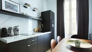 Cozinha moderna com forno embutido, cafeteira e micro-ondas. Há uma mesa de jantar com cadeiras e um vaso com planta sobre a mesa.