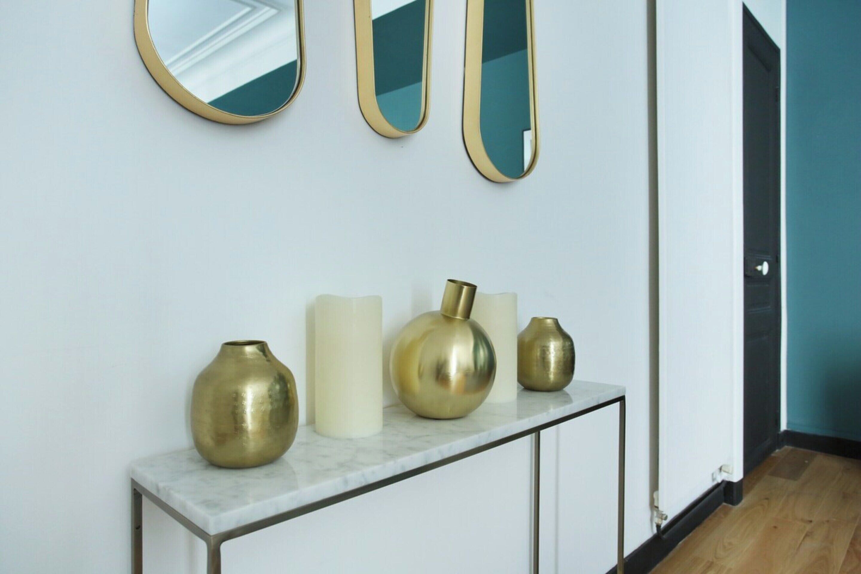 A hallway with a white wall, a marble console table with vases, and three mirrors.