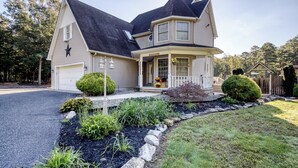 A two-story house with a garage, a covered porch, and a landscaped front yard with a stone border and various plants. - ClubDivot - A Modern Farm Style  Home with Pool and Backyard Bar (Vineland)
