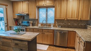 A kitchen with wooden cabinets, a stainless steel dishwasher, a double sink, and a stove. - ClubDivot - A Modern Farm Style  Home with Pool and Backyard Bar (Vineland)