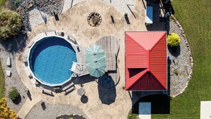 An aerial view of a backyard with a swimming pool, a red-roofed structure, and a wooden deck. - ClubDivot - A Modern Farm Style  Home with Pool and Backyard Bar (Vineland)