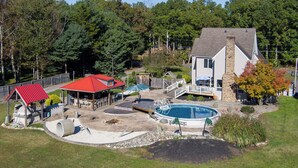 A residential property with a swimming pool, a covered patio, and a house with a stone chimney. - ClubDivot - A Modern Farm Style  Home with Pool and Backyard Bar (Vineland)
