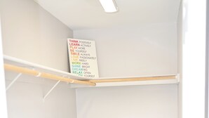 Un armario ordenado con estantes y barra para colgar, un tapete azul en el suelo, y una frase motivadora en la pared.