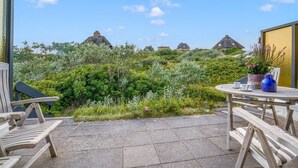 A patio with a table and chairs, overlooking a lush garden and traditional houses. - Haus Hildebrand - "Relax and feel good in Haus Hildebrand!" (Hörnum)