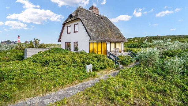 A white house with a thatched roof, surrounded by lush greenery and a clear sky. - Haus Hildebrand - "Relax and feel good in Haus Hildebrand!" (Hörnum)