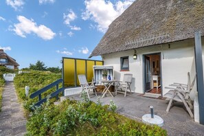 A thatched-roof house with a patio area, outdoor seating, and a view of the surrounding landscape.