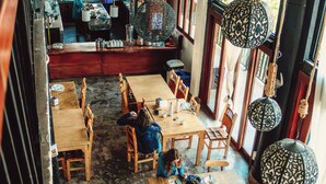 Un restaurante con mesas y sillas de madera, un balcón con bicicletas y faroles colgantes.