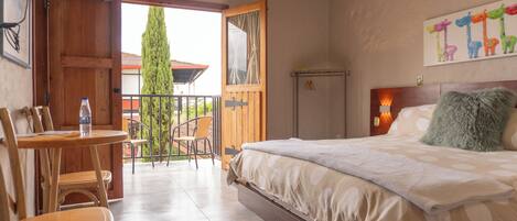 A bedroom with a bed, a table with chairs, a balcony, and a painting on the wall.
