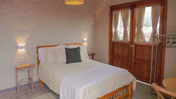 A bedroom with a wooden bed, two bedside tables, a hanging light fixture, and a wooden wardrobe with curtains.