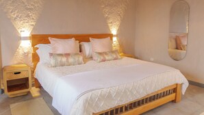 Un dormitorio con cama de madera, ropa de cama blanca y una mesita de noche con lámpara.