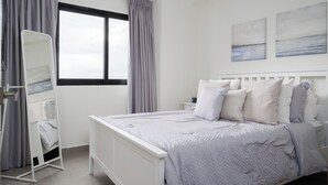 Une chambre bien rangée, avec un lit, une table de chevet, un miroir et une fenêtre avec des rideaux.