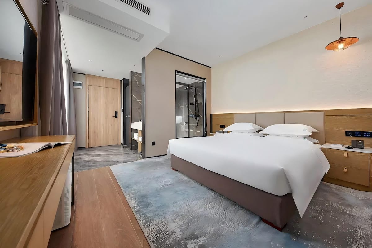 A modern hotel room with a large bed, wooden furniture, a desk, and a walk-in closet.