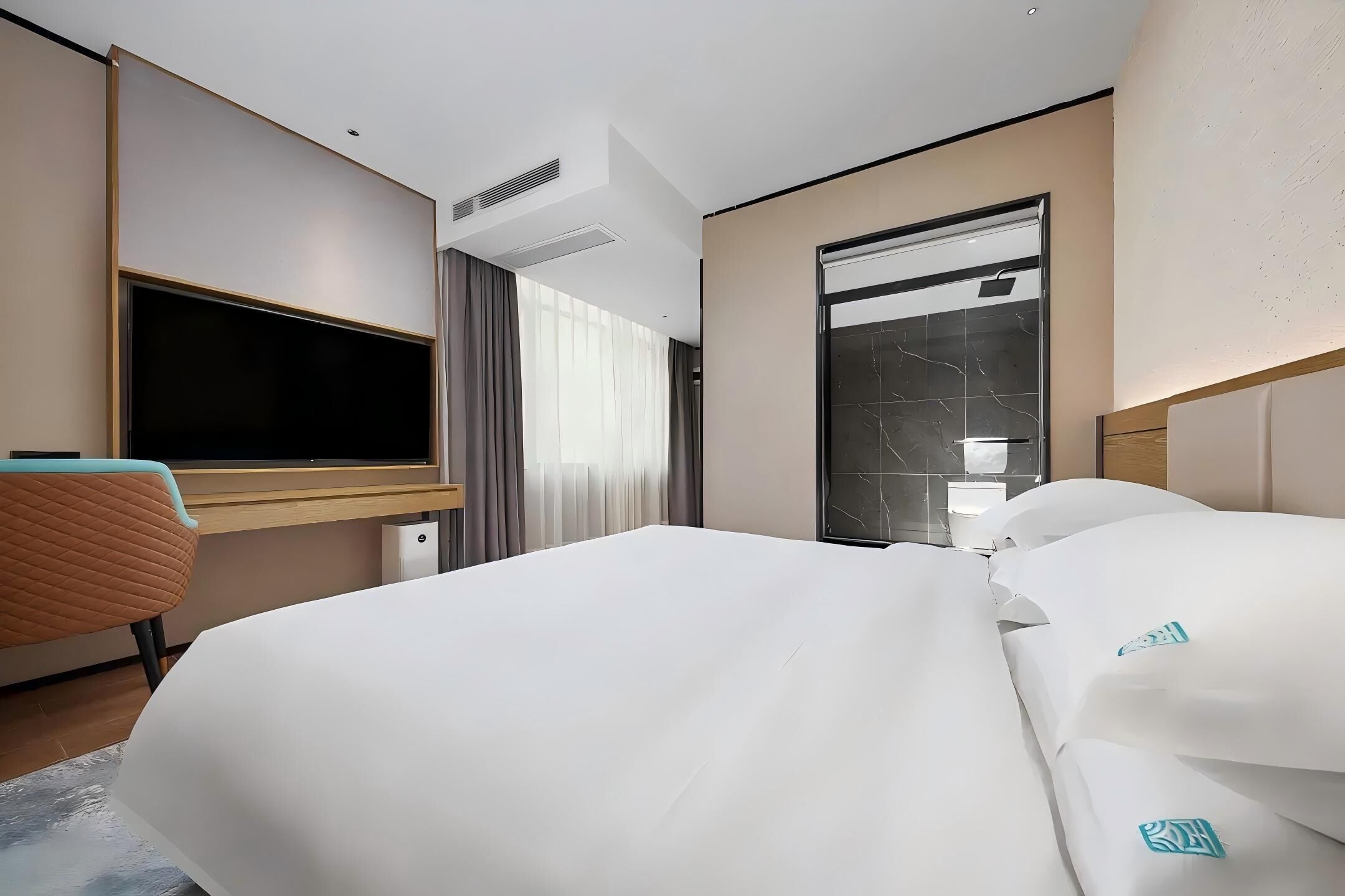 Hotellihuone, jossa on suuri sänky, työpöytä tuolilla, taulutelevisio ja suuri ikkuna, jossa on verhot.
