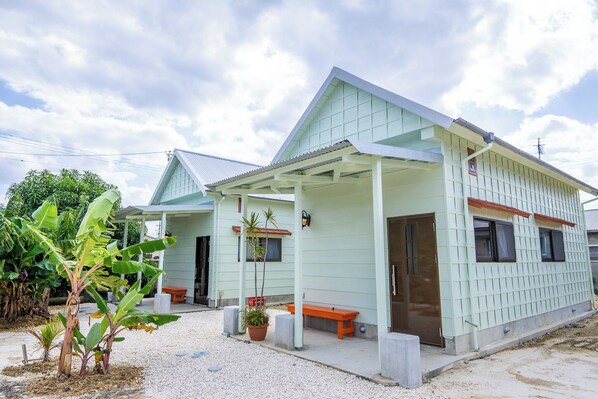A light green building with a covered porch, a bench, and potted plants. - CORAZON RESORT (Minamidaito)