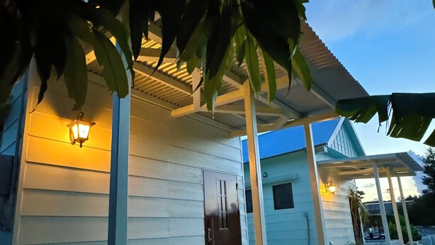 A house with a covered porch, a door, and a small garden area with potted plants. - CORAZON RESORT (Minamidaito)