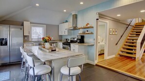 A modern kitchen with a marble island, white chairs, and a built-in stove.