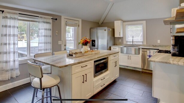 A modern kitchen with a central island, white cabinetry, and a stainless steel refrigerator.