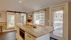A kitchen with a marble countertop, a microwave, and a sink. There is a dining table with chairs and a vase of flowers.