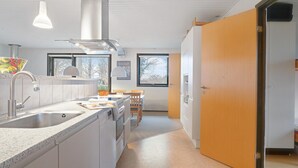 A modern kitchen with a built-in oven, a sink, and a dining area with a table and chairs. - Lovely home in Samsø with WiFi (Samsø)
