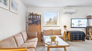 A cozy living room with a beige sofa, a wooden coffee table, and a bookshelf filled with books and decorative items. - Lovely home in Samsø with WiFi (Samsø)