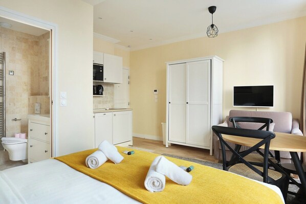 A hotel room with a bed, a yellow towel, a TV, a sofa, and a dining table.