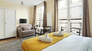 A hotel room with a bed, a sofa, a table, and chairs. There are curtains on the windows, and a TV is mounted on the wall. - Lovely Studio With AC - Center of Paris (Paris)