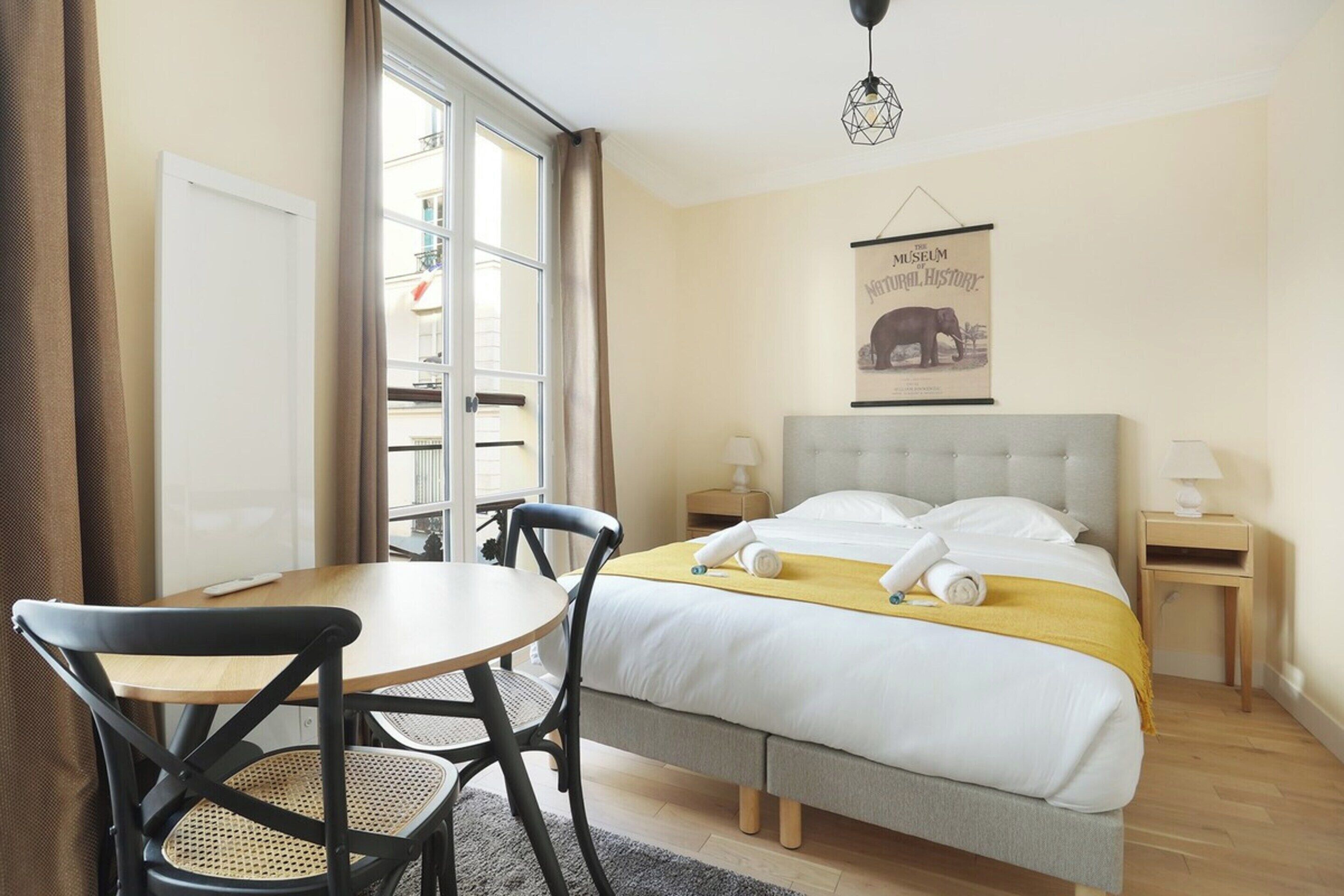 Una habitación de hotel con una cama, una mesa, sillas, una ventana y un cartel colgado en la pared.