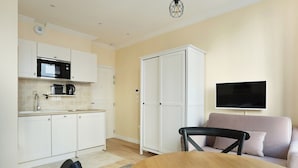 A modern kitchen with white cabinets, a microwave, and a coffee maker. There is a dining table with chairs and a sofa in the living area. A flat-screen TV is mounted on the wall. - Lovely Studio With AC - Center of Paris (Paris)