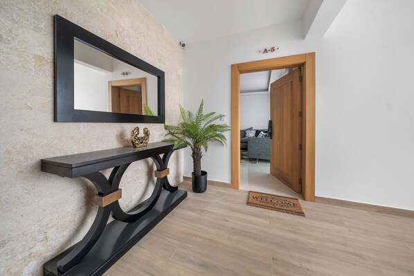 A modern interior with a console table, a potted plant, a mirror, and a wooden door leading to another room. - Hermoso Apart en el Bello Santiago (Santiago de los Caballeros)
